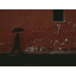  A Man Carrying an Umbrella Walks Alongside a Red Wall 